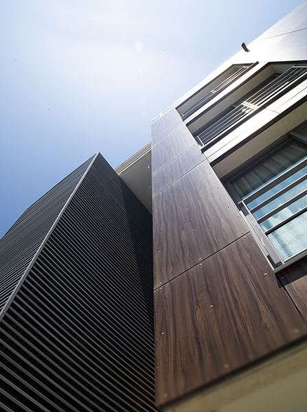 Vue en contre-plongée d'un bâtiment moderne avec une façade à rayures sombres et des murs lambrissés.