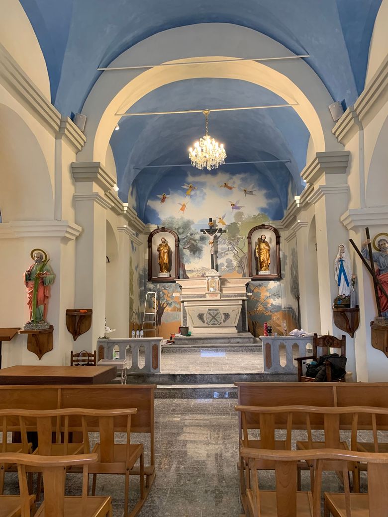 Intérieur d'une église. Plafond voûté bleu, autel avec crucifix, tableaux et bancs en bois.