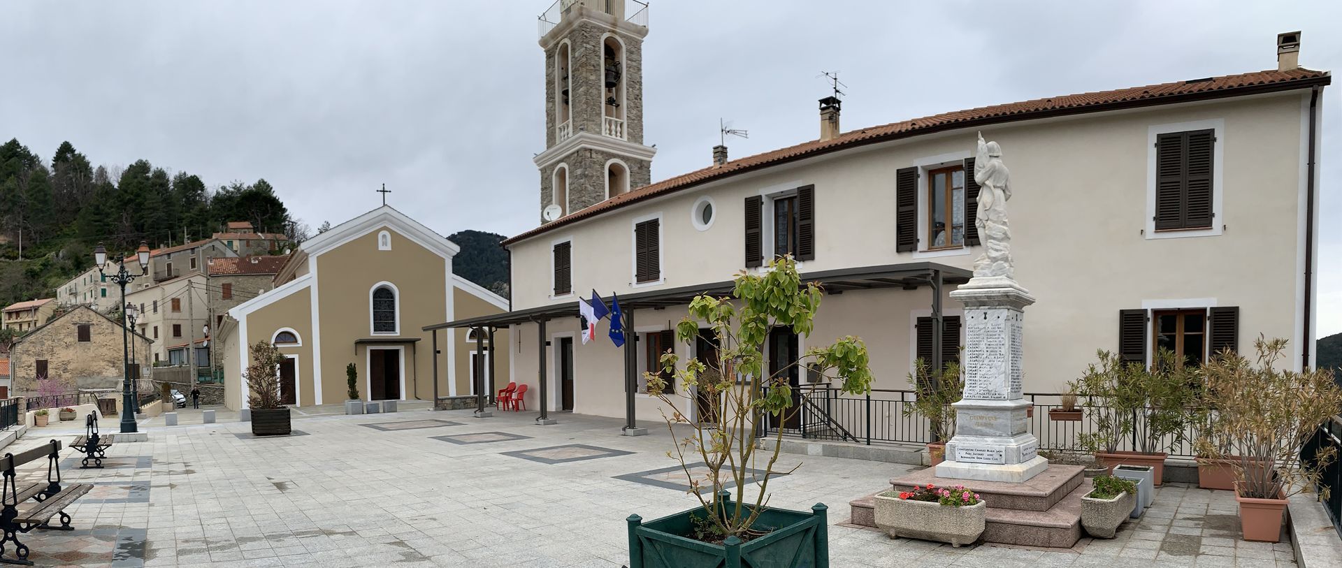 Une place de village comprenant une église, une tour, des bâtiments et une statue.