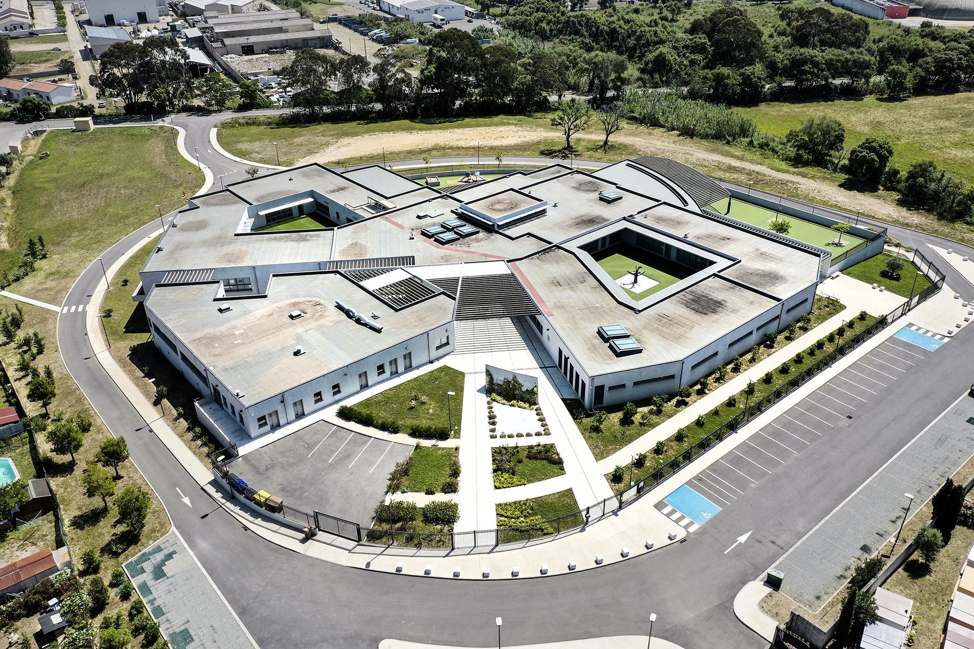 Vue aérienne d'un bâtiment moderne à plusieurs ailes, avec une allée circulaire et un parking environnant.