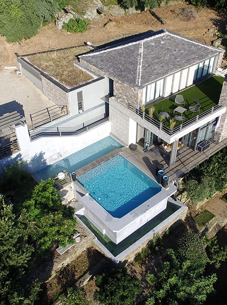 Maisons à flanc de colline surplombant la mer, encadrées d'arbres et d'une balustrade en bois.