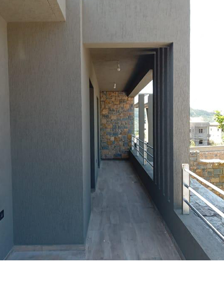 Un couloir gris avec un sol en bois s'ouvre sur un mur de pierre et un balcon avec une balustrade en métal.