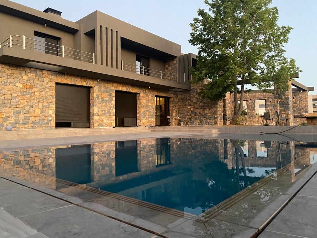 Maison moderne avec piscine reflétant la structure et un arbre, coucher de soleil.