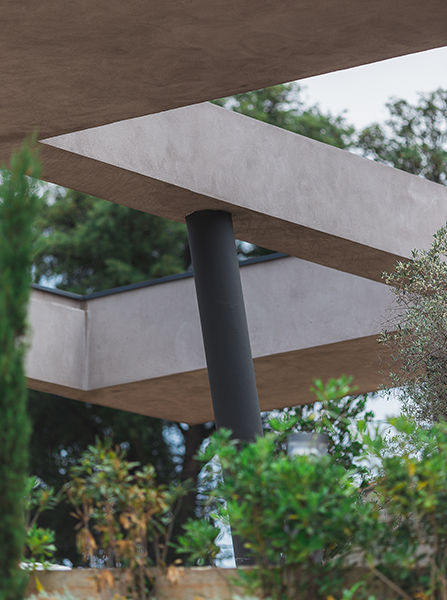 Bâtiment en béton gris avec colonne sombre, entouré de feuillage vert.