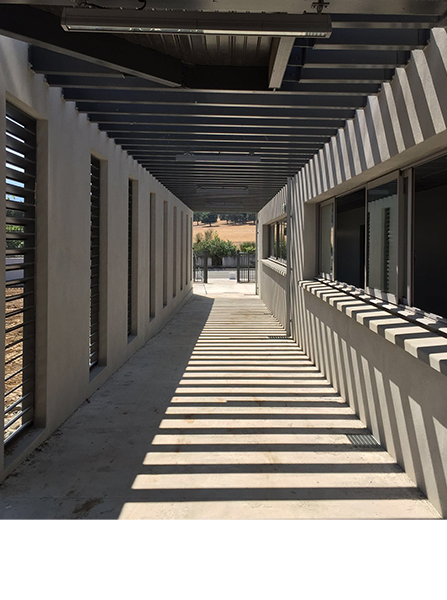 Passerelle en béton avec toit à lattes projetant des ombres.
