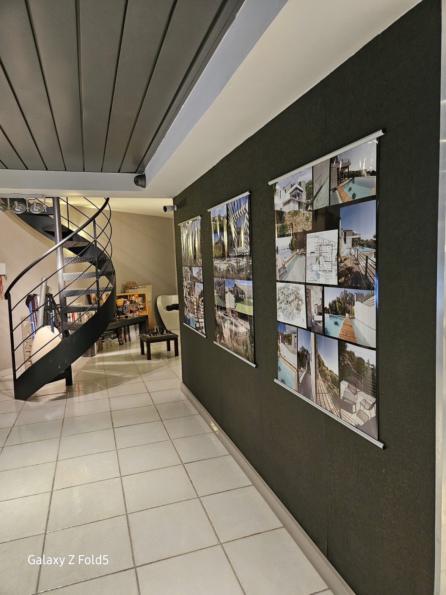 Couloir avec escalier en colimaçon et exposition de photos sur un mur sombre.