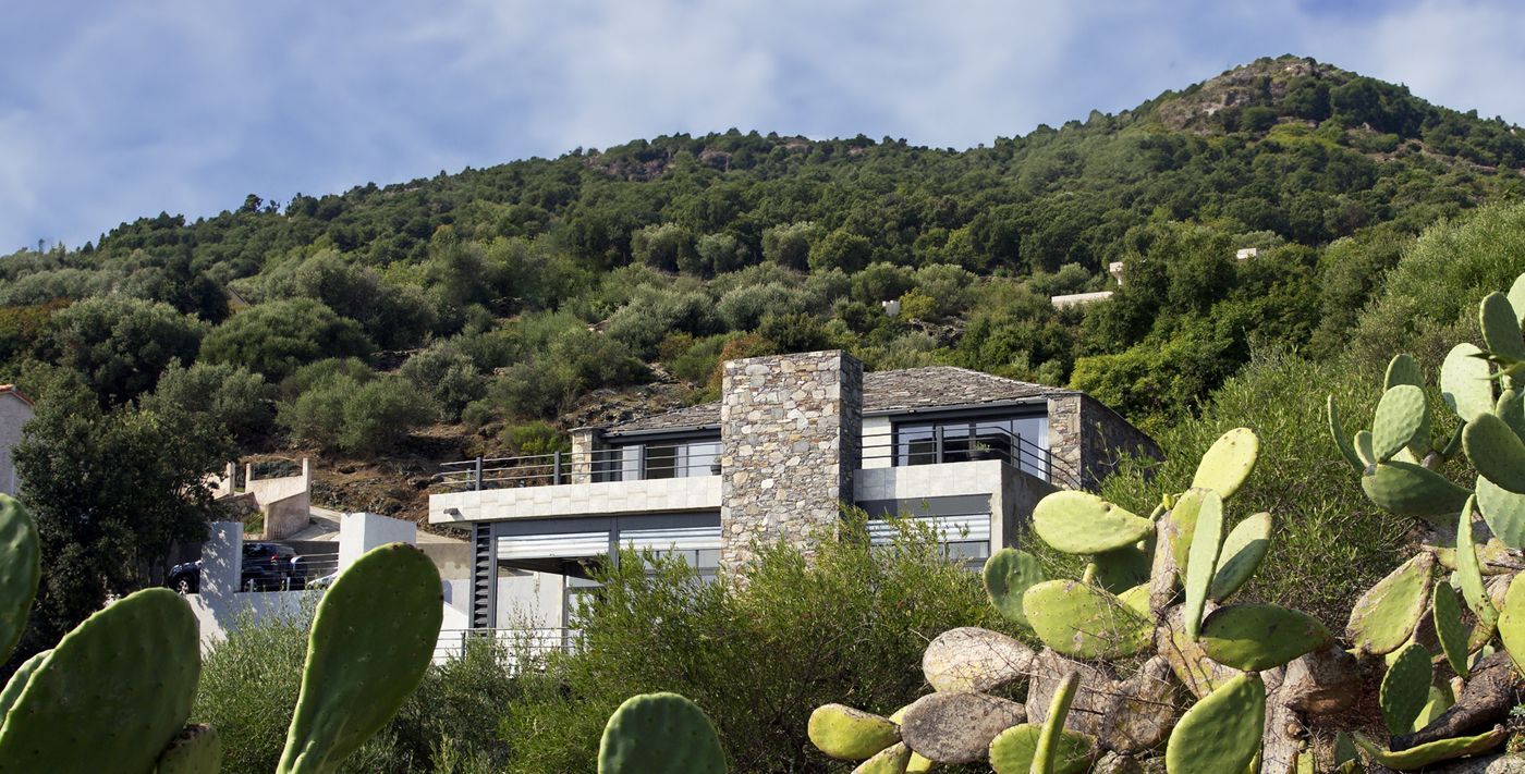 Maison en pierre moderne nichée au milieu d'une montagne verdoyante avec des cactus.