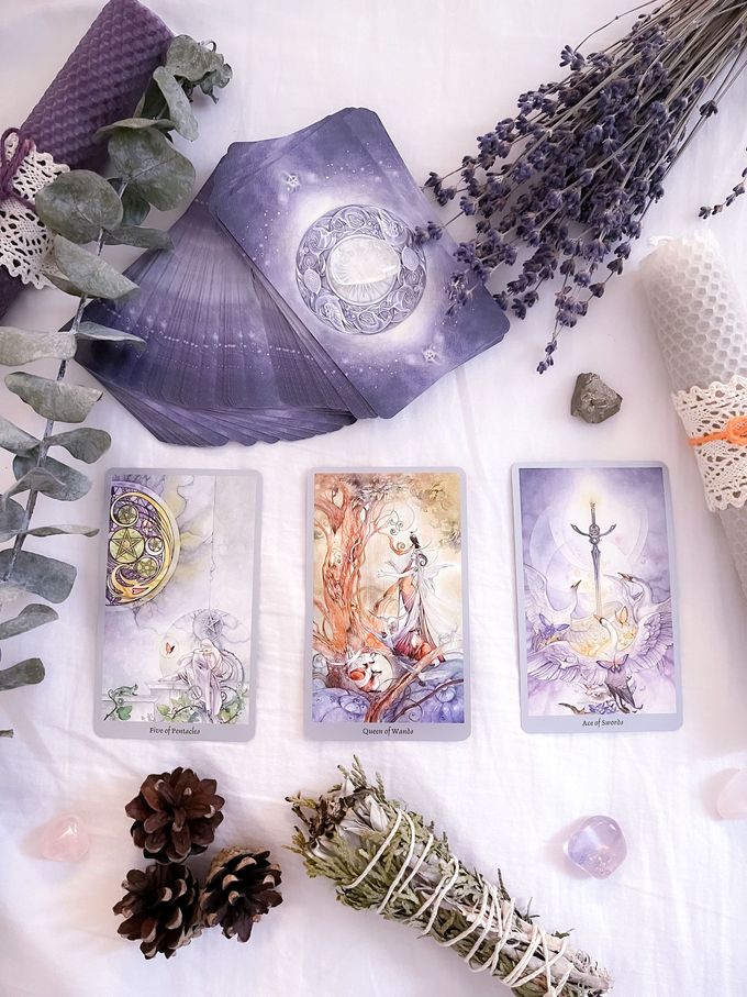 Altar de cristal morado y flores con cartas del tarot, salvia, lavanda y piñas sobre un fondo blanco.