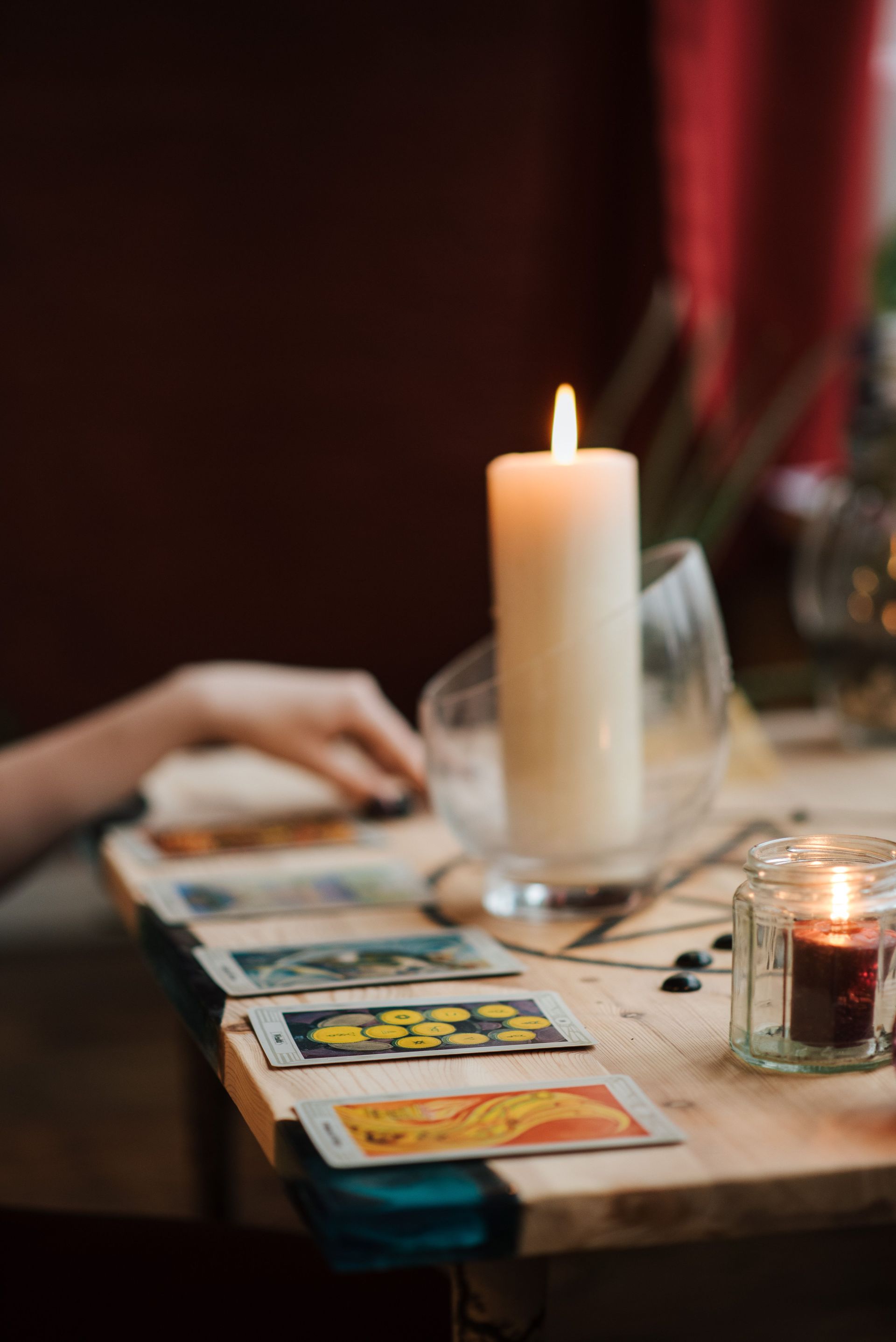 Una vela encendida sobre una mesa acogedora con cartas del tarot, una mano descansando cerca y una pequeña vela 