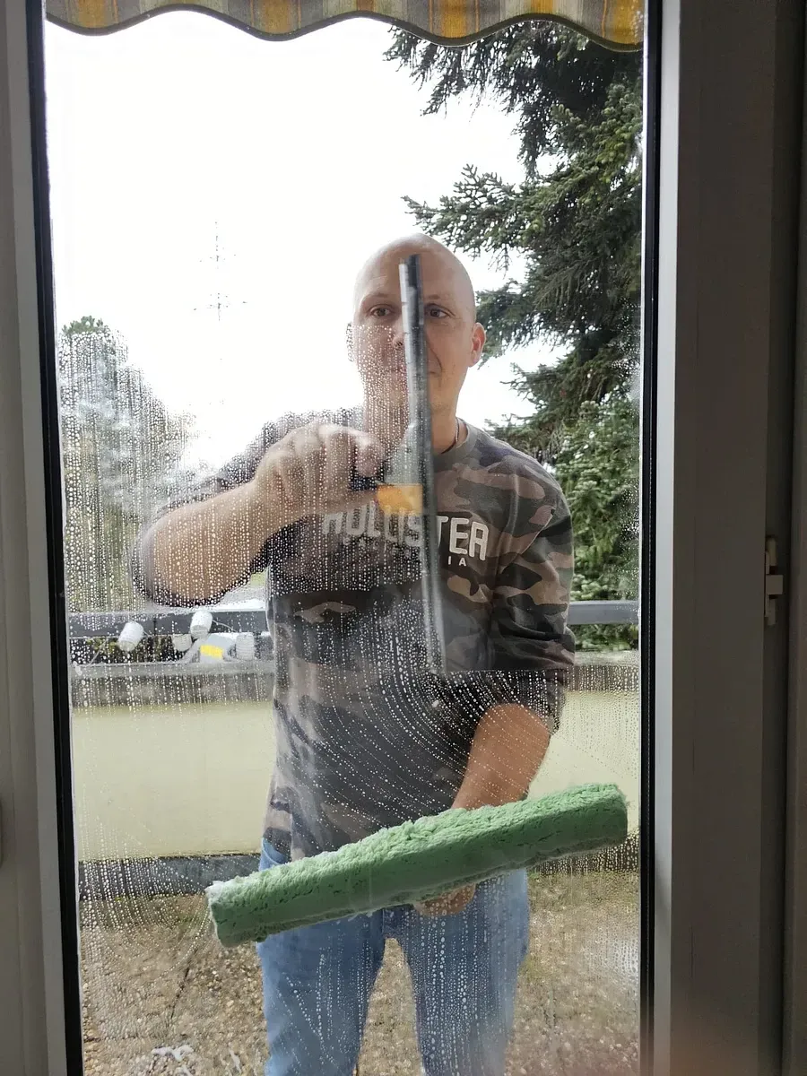 Un homme nettoie une fenêtre avec une raclette.