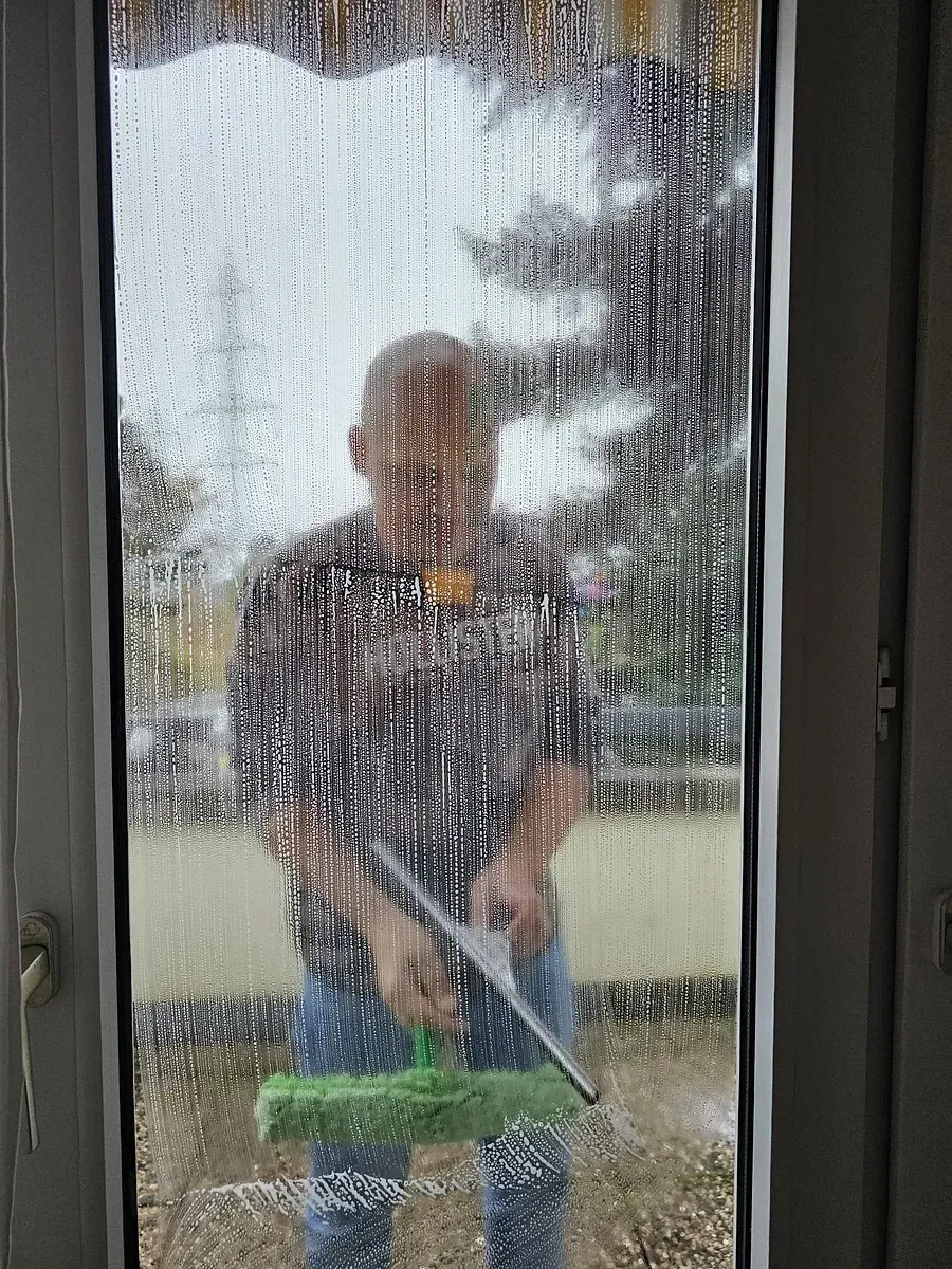 Un homme nettoie une fenêtre avec une raclette.