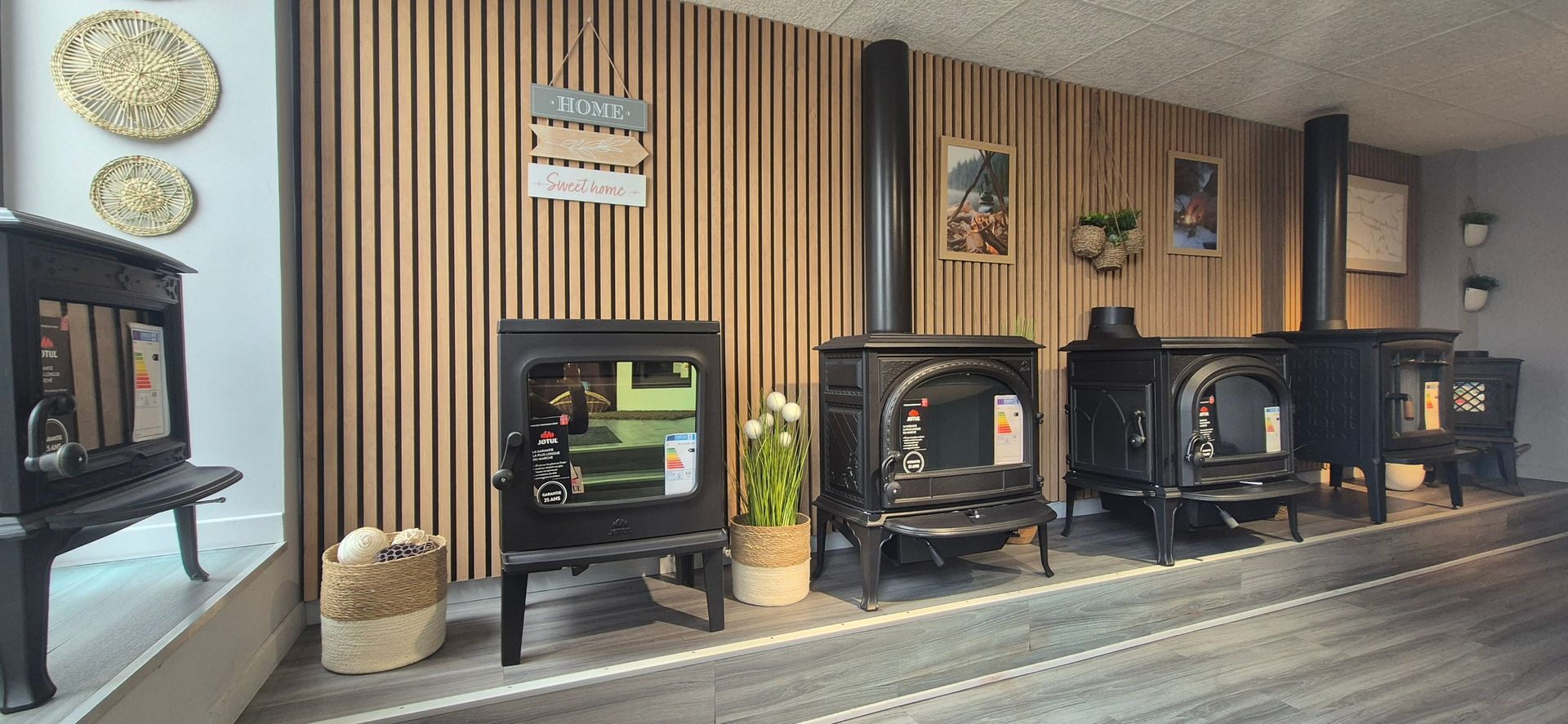 Rangée de poêles à bois noirs présentés contre un mur en bois dans une salle d’exposition.