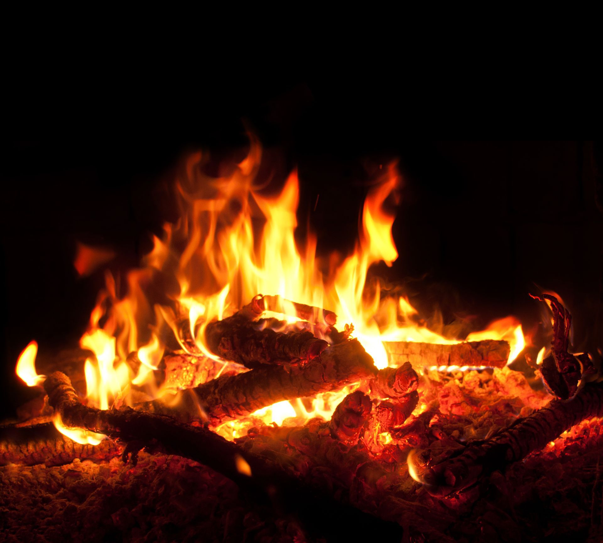 Des flammes orange incandescentes brûlent au-dessus d'un lit de braises dans une cheminée sombre.
