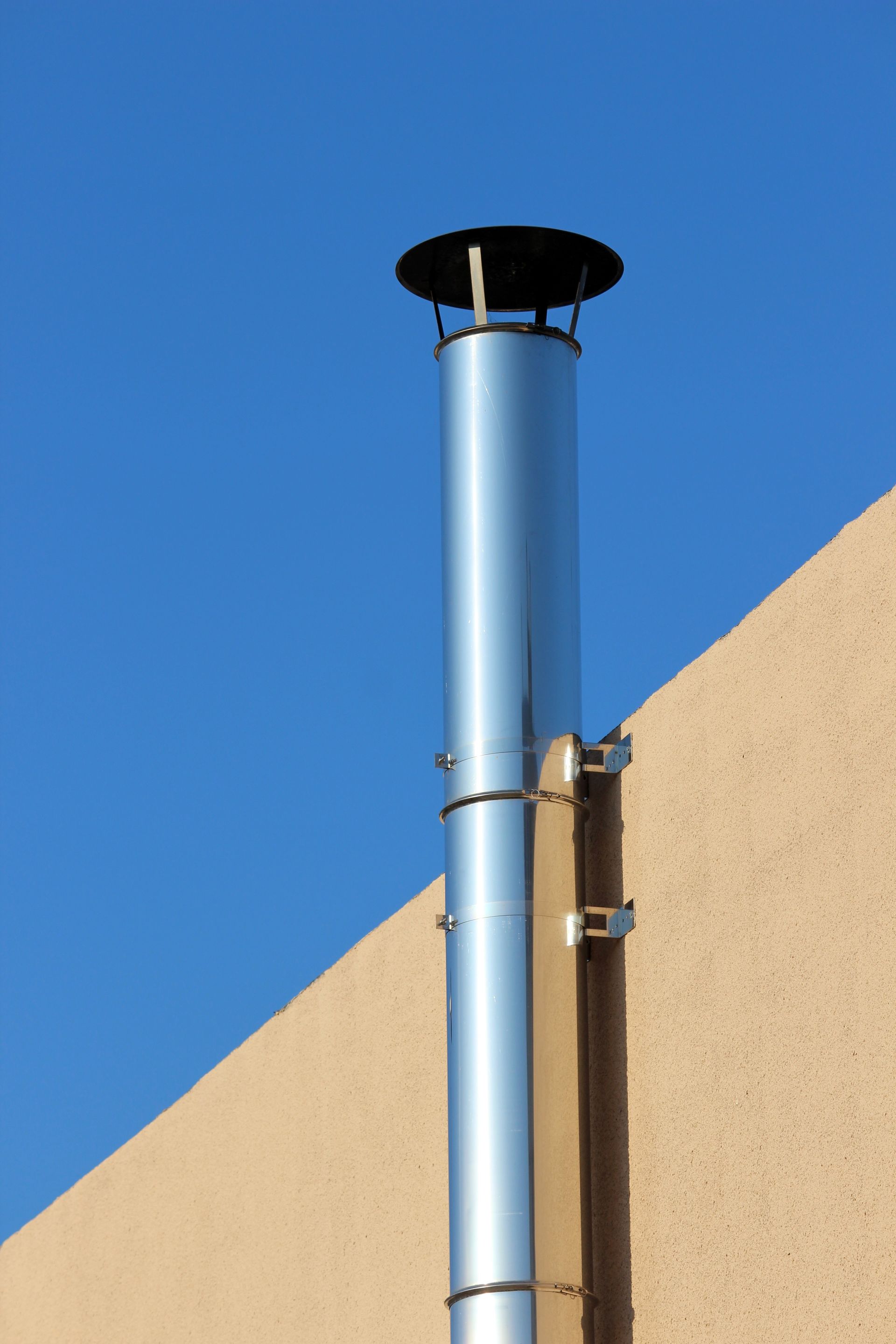 Conduit de cheminée en métal argenté sous un ciel bleu et un mur beige.