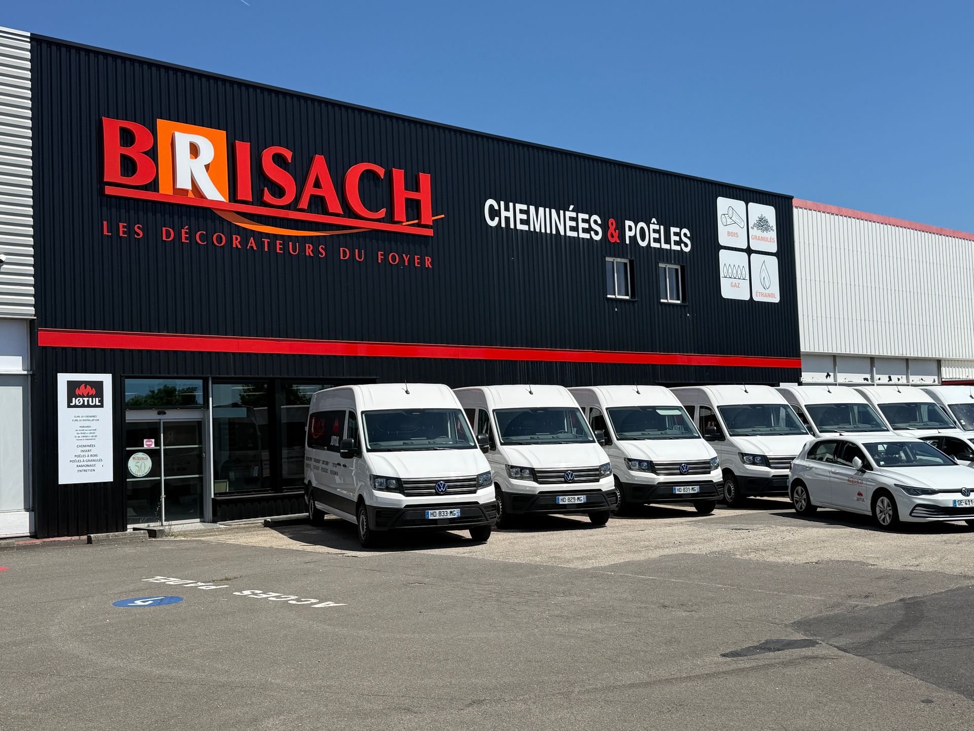Magasin Brisach avec une enseigne rouge sur fond noir, des camionnettes et voitures blanches garées devant.