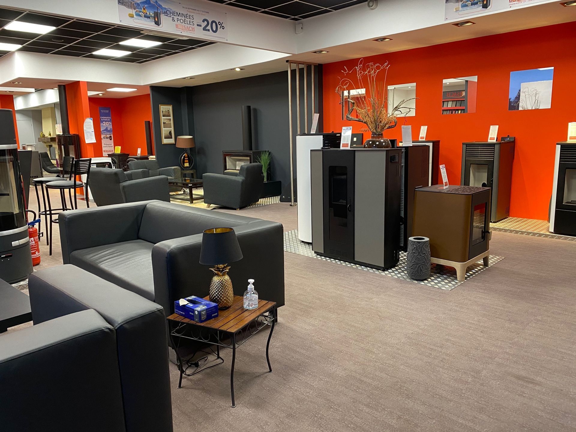 Showroom avec des canapés gris, des fauteuils, des poêles dans un décor aux murs rouges.
