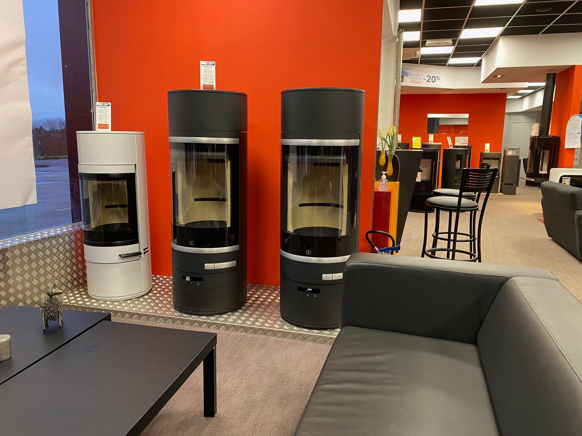 Une pièce du showroom avec 3 modèles de poêles contre un mur rouge.
