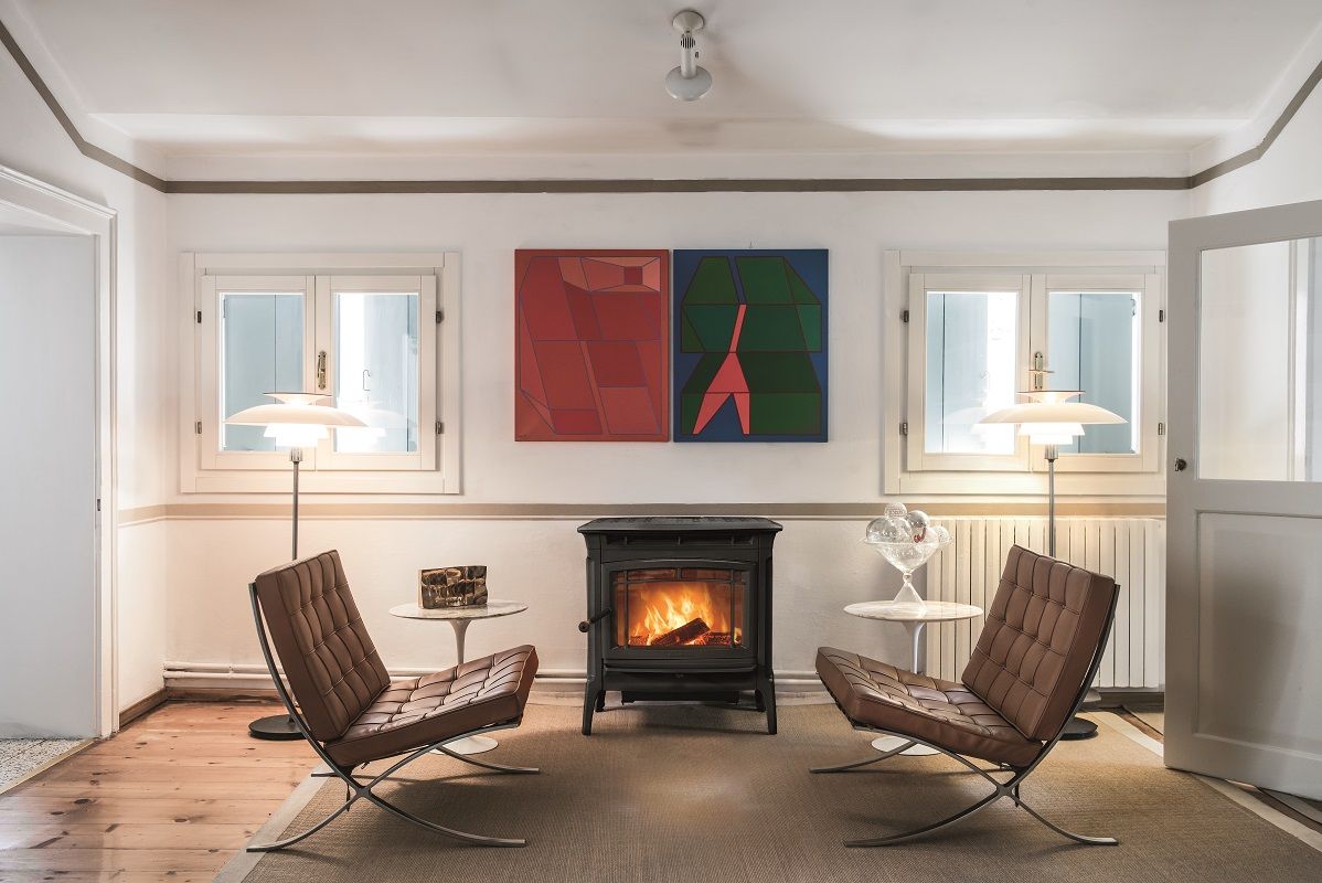 Salon moderne avec deux fauteuils face à un poêle à bois allumé et une œuvre d’art abstraite au mur.