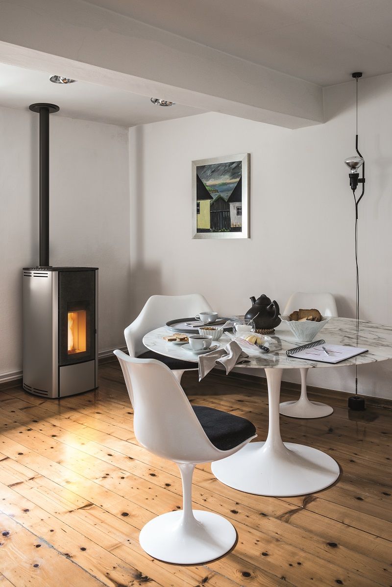 Salle à manger moderne avec poêle à granulés, table ronde blanche et chaises blanches sur un parquet en bois.
