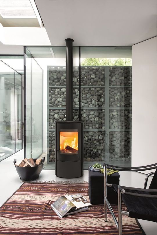 Salon moderne avec un poêle à bois, une paroi vitrée et un tapis à motifs.