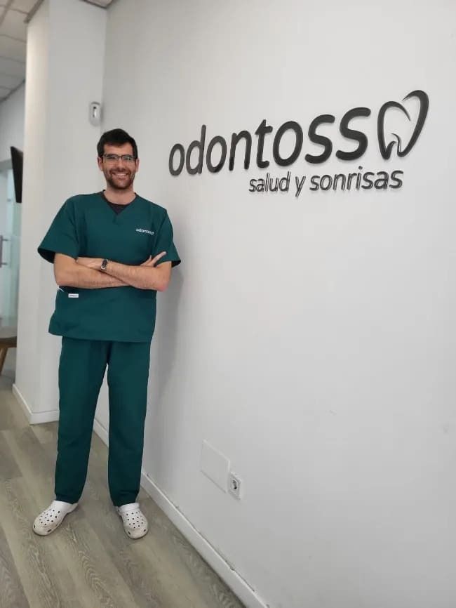 Un hombre con uniforme médico está parado frente a un cartel que dice odontoss