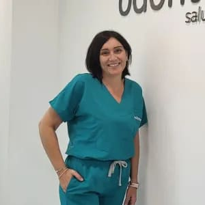 Una mujer con uniforme médico está parada frente a una pared blanca.