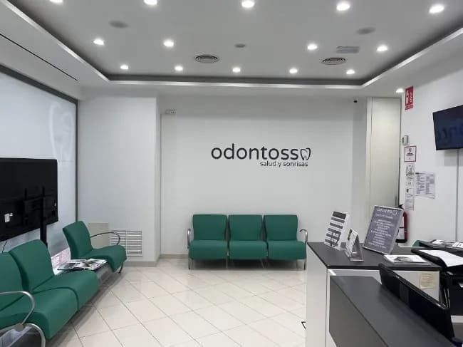 Una sala de espera con sillas verdes y un cartel que dice odontossi
