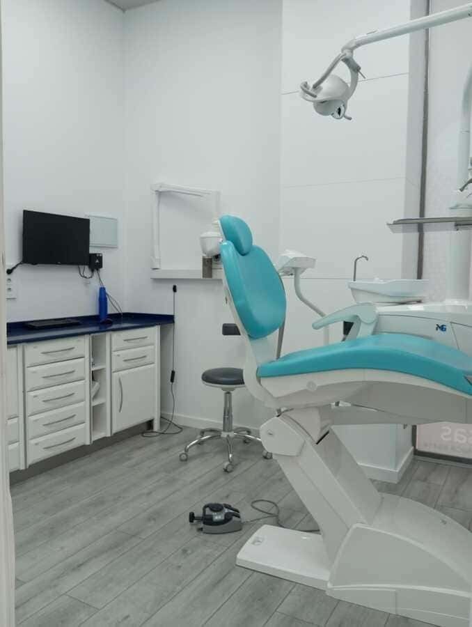 Un consultorio dental con un sillón dental azul y un monitor en la pared.