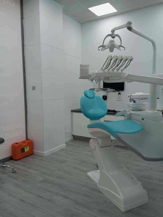Un consultorio dental con un sillón dental azul y equipo dental.