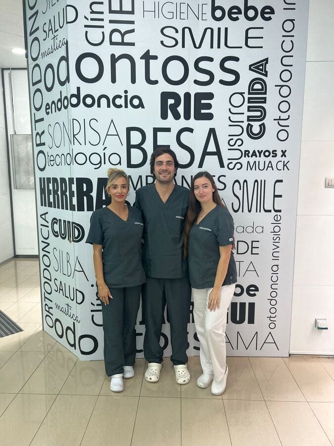 Un hombre y dos mujeres posan para una foto frente a una pared con palabras en español.