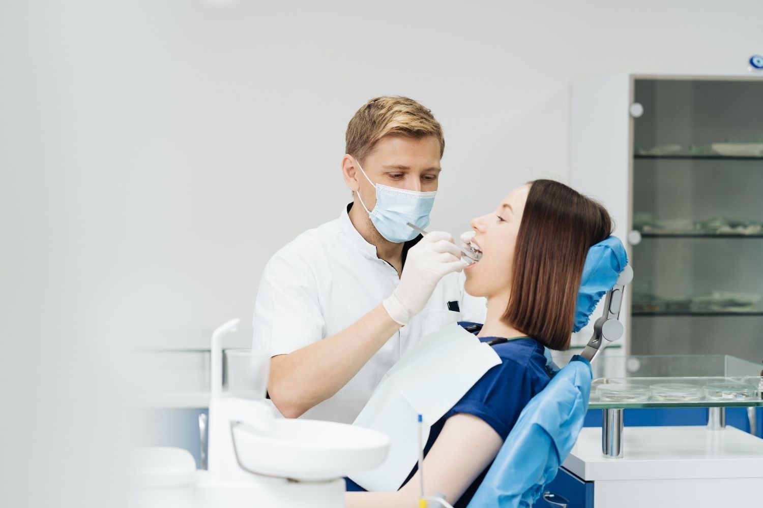 Una mujer está sentada en una silla dental mientras un dentista le examina los dientes.