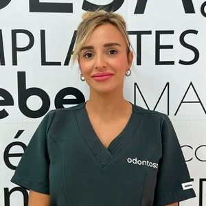 Una mujer con una blusa verde está parada frente a un cartel que dice Pilates.
