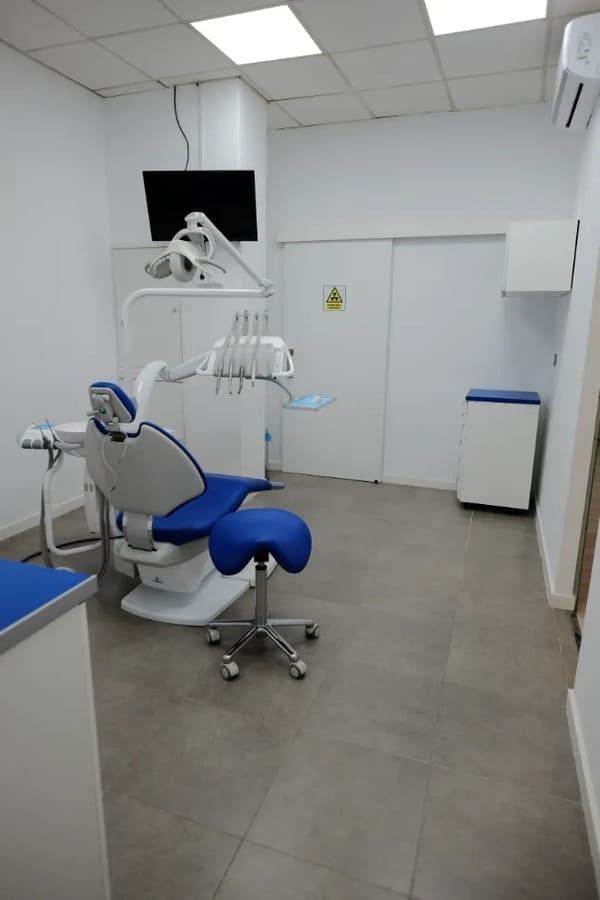 Un consultorio dental con un sillón dental azul y un televisor en la pared.