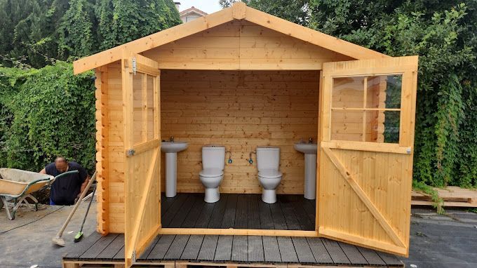 Un cobertizo de madera con dos inodoros y dos lavabos.