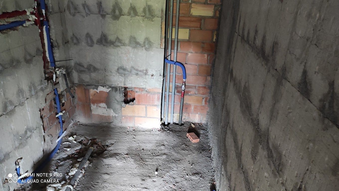 Un baño en construcción con pared de ladrillo y tuberías azules.