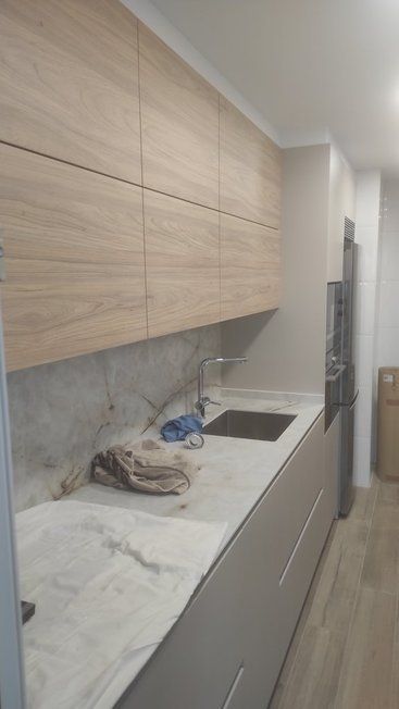 Una cocina con gabinetes de madera, encimeras de mármol, un fregadero y un refrigerador.