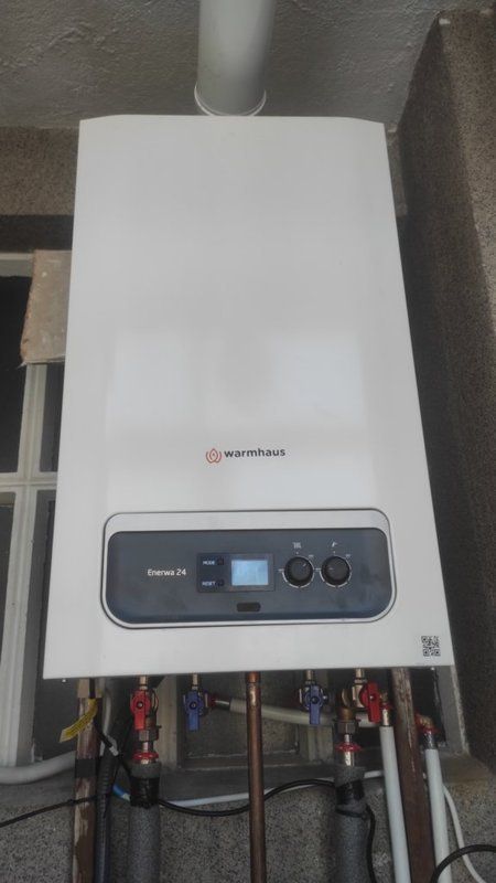 Una caldera blanca está colocada encima de una tubería de cobre.