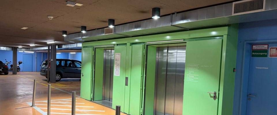 Grüne Aufzugtüren in einem Parkhaus mit blauen Wandpaneelen und Deckenleuchten