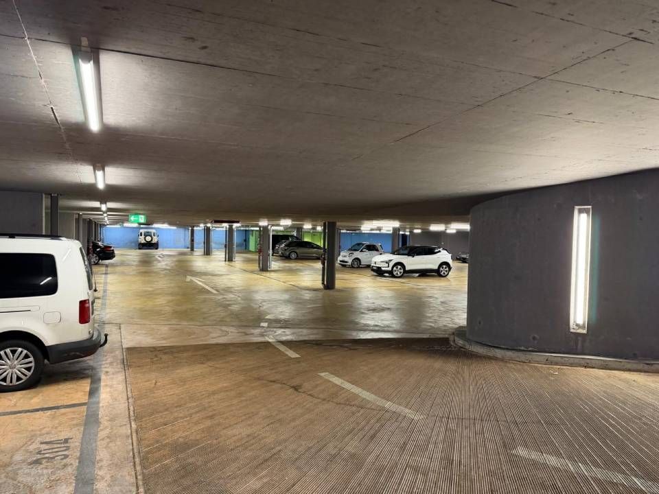 Tiefgarage mit geparkten Autos, Betonpfeilern und Leuchtstoffröhren an der Decke.