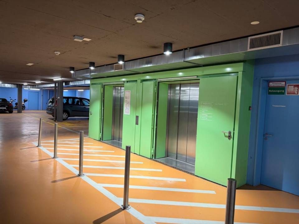 Grüne Aufzugtüren in einer Tiefgarage mit orangefarbenen Bodenmarkierungen