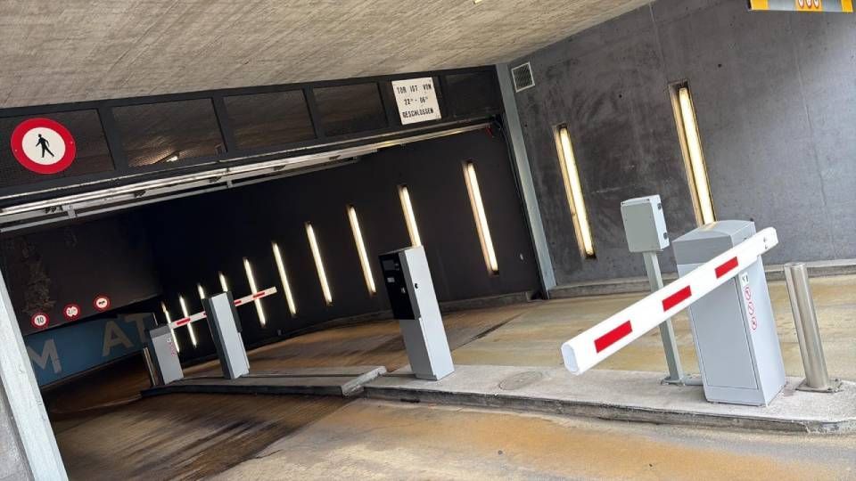 Leerer Tiefgarageneingang mit Schranke und Ticket-/Zahlungsautomaten auf einer Betonrampe.