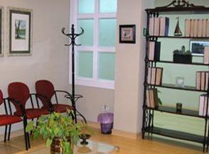 Una sala de espera con sillas rojas y una estantería llena de libros.