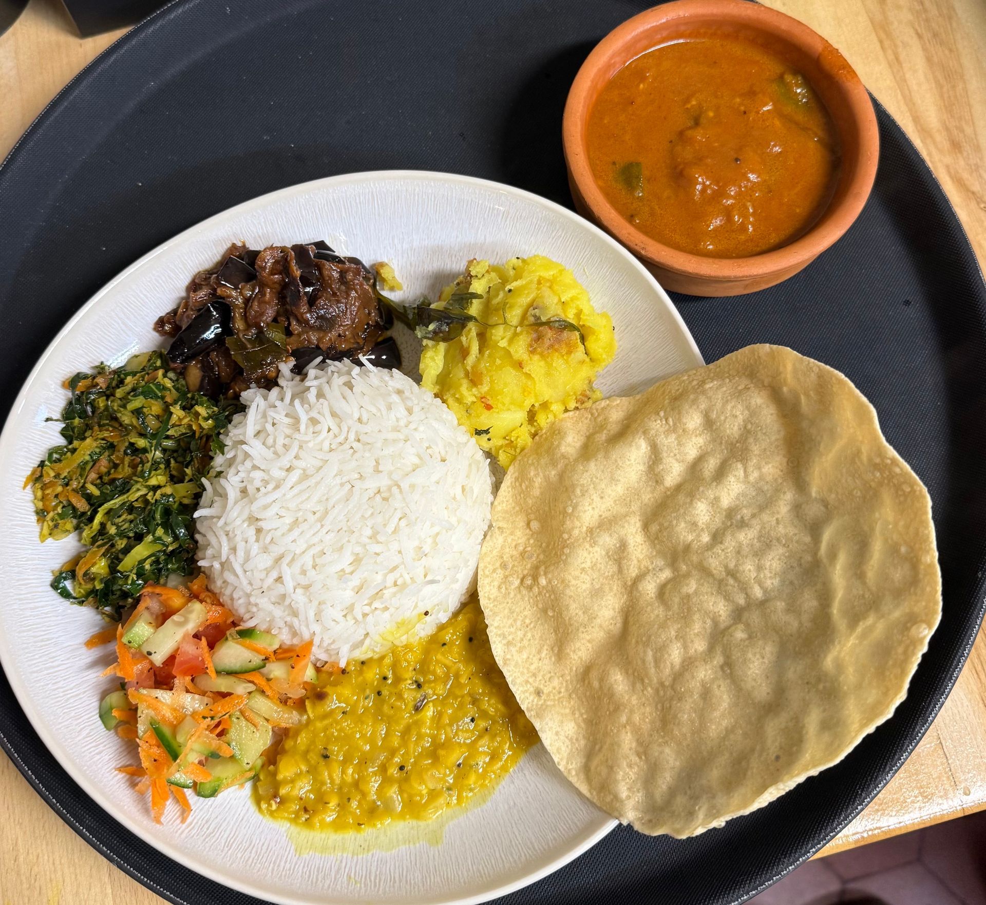 Vier Lattes mit herzförmiger Schaumkunst auf Untertassen, platziert auf einem Holztisch mit umliegenden Topfpflanzen.