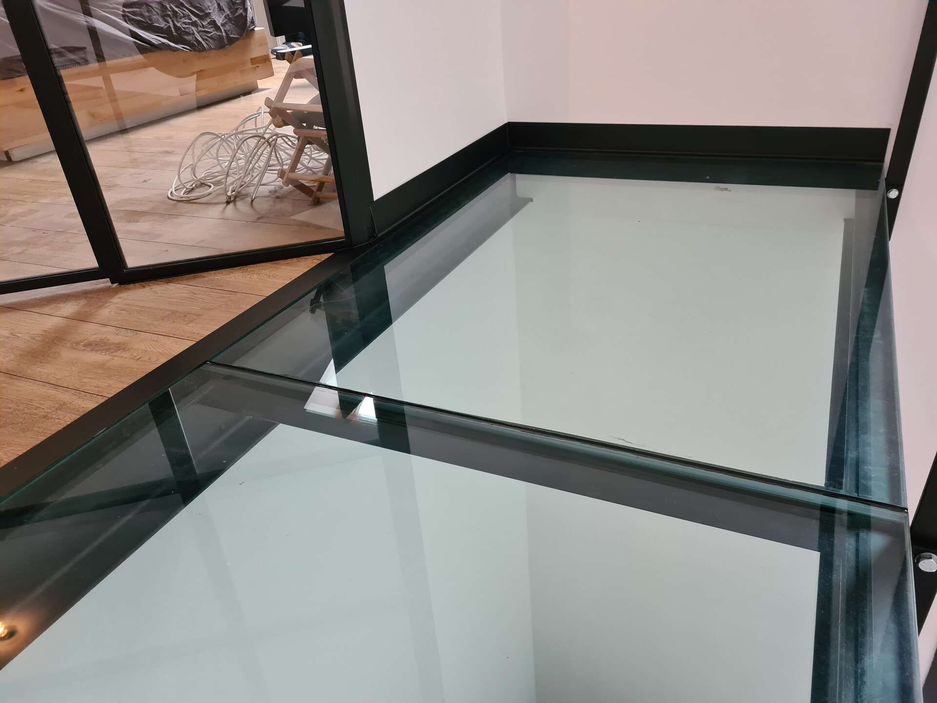 Panneaux de verre au sol, à côté d'une terrasse en bois et d'une paroi vitrée à cadre noir, dans un intérieur moderne