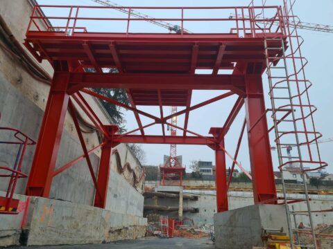 Échafaudage en acier rouge au-dessus d'un chantier de construction en béton, avec une échelle sur la droite