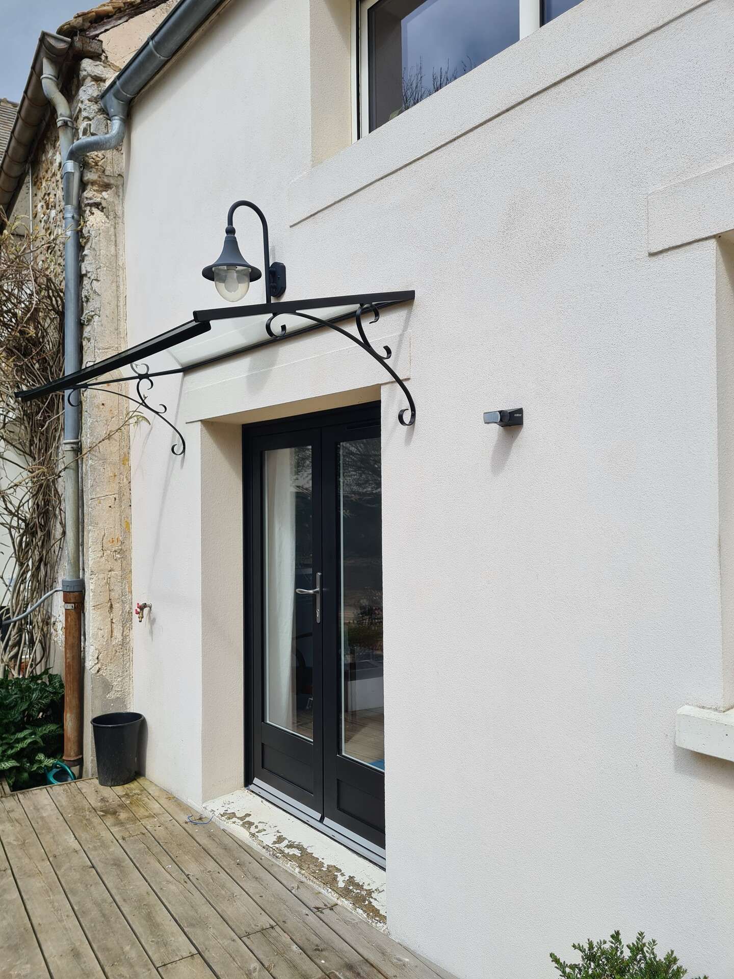 Porte d'entrée extérieure avec portes vitrées à cadre noir et marquise en métal noir.