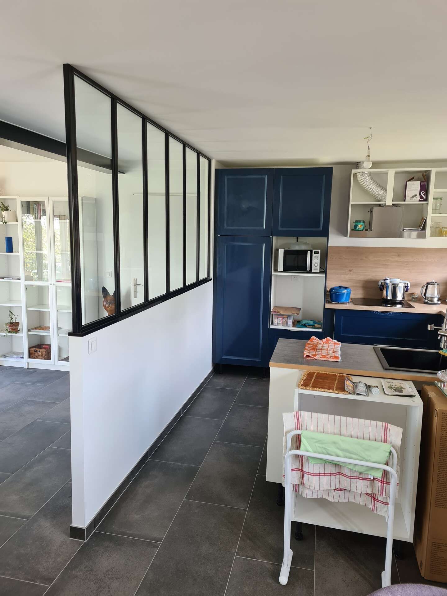 Cuisine moderne avec placards bleus, cloison vitrée à cadre noir et petit îlot central.