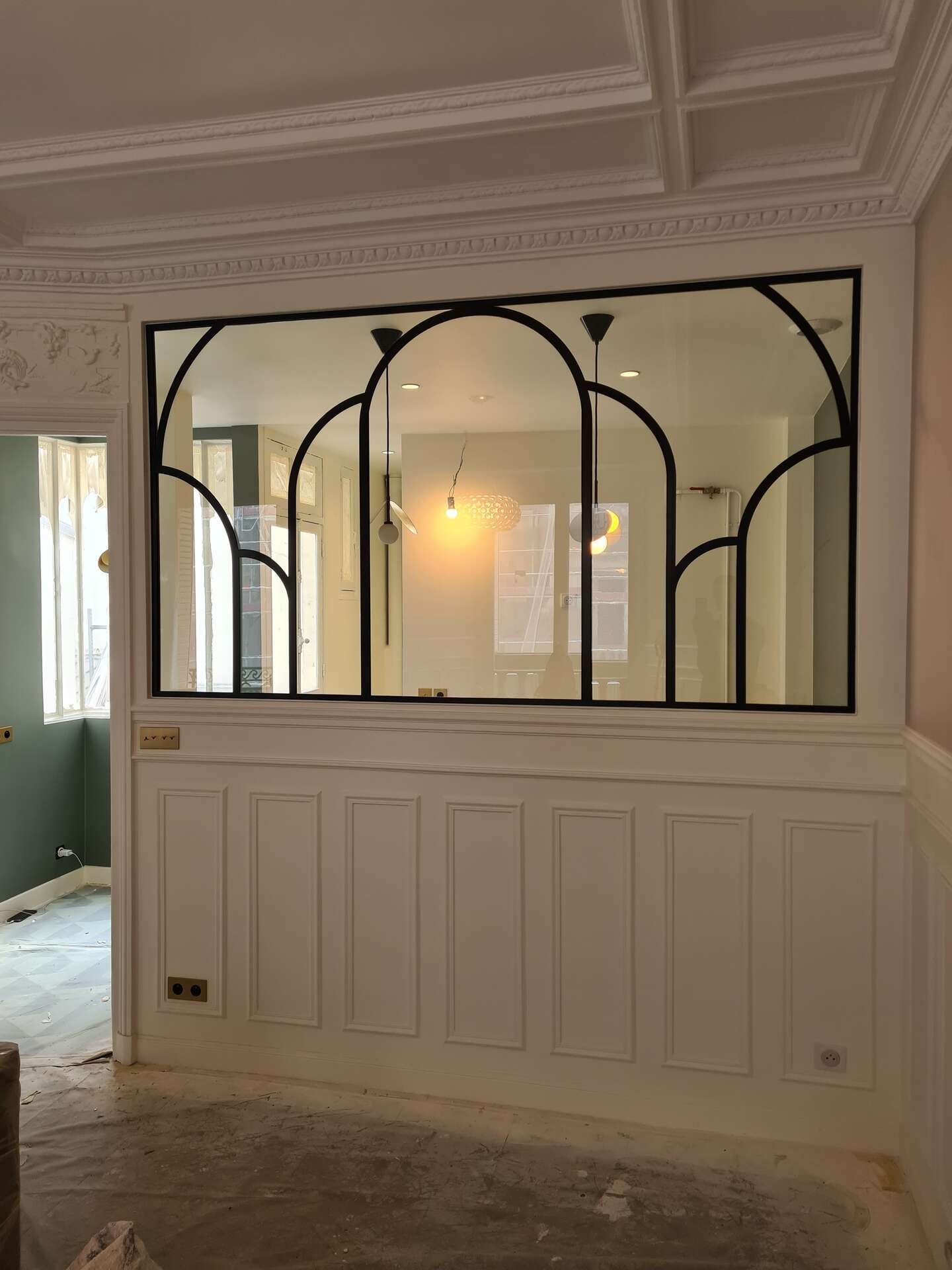 Cloison intérieure avec une séparation noire de style fenêtre cintrée au-dessus d'un lambris blanc.