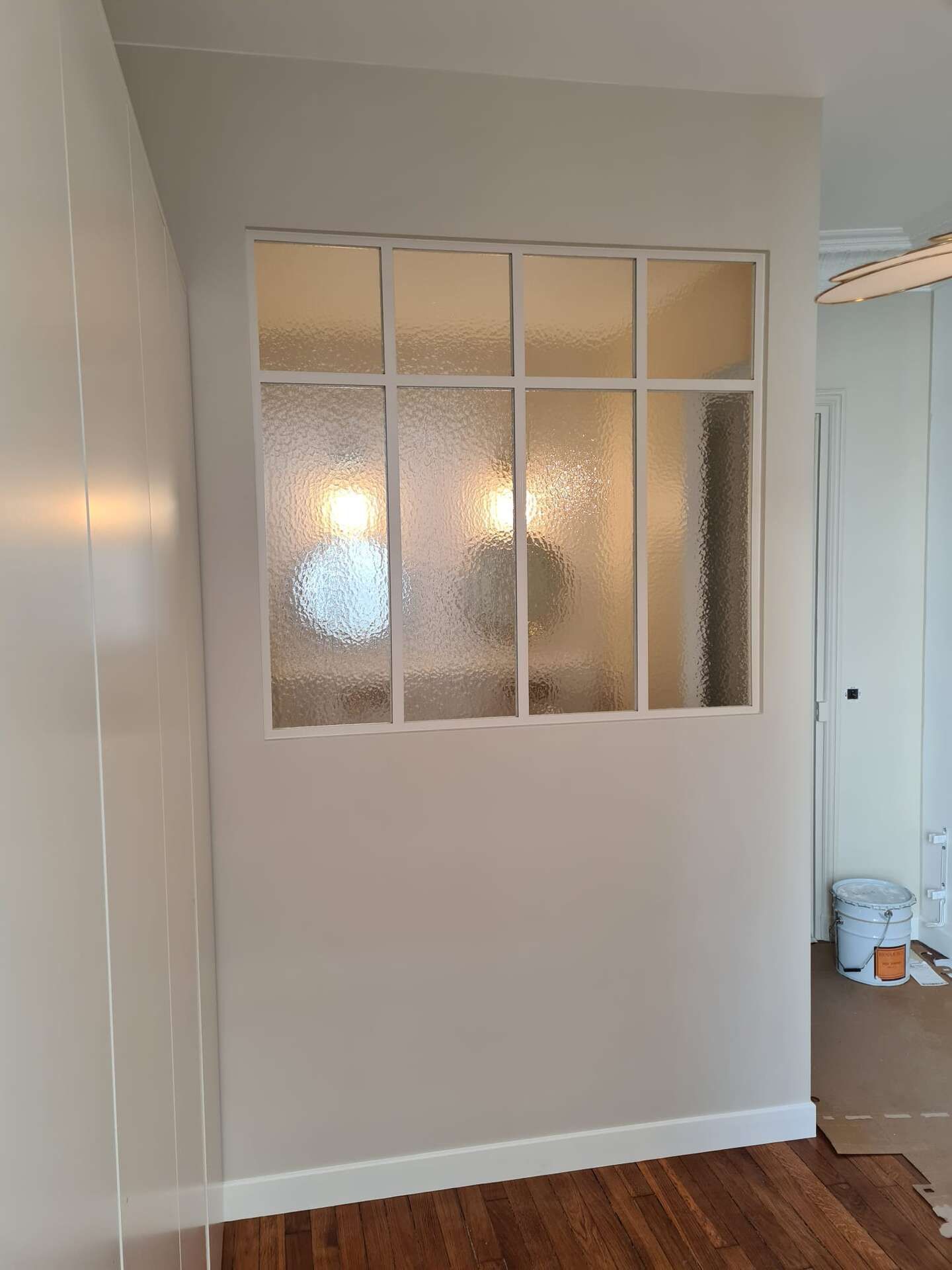 Petite pièce avec des panneaux de fenêtres en verre dépoli, des murs beiges et un parquet.