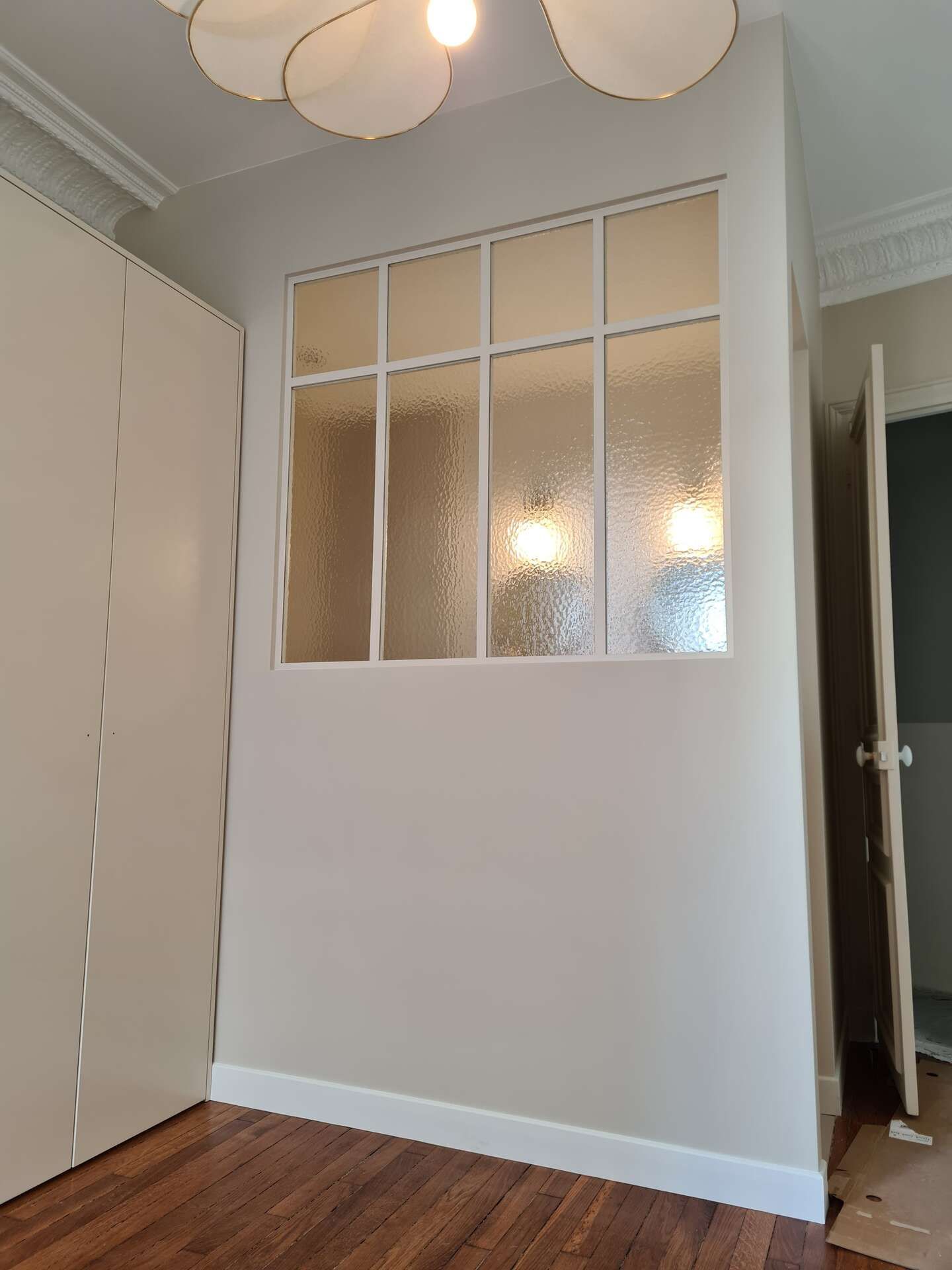 Petite pièce avec des panneaux de verre dépoli, des murs blancs, un parquet et un plafonnier.